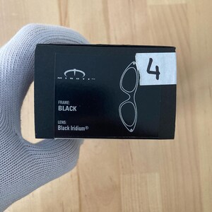 May include: Black eyewear box with the text "MINUTE" and a diagram of the glasses. The box also has the text "FRAME: BLACK" and "LENS: Black Iridium&reg;". A white sticker with the number "4" is on the box.