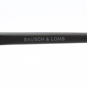 May include: Close-up of the black arm of a pair of glasses with the text "BAUSCH & LOMB" printed in white.