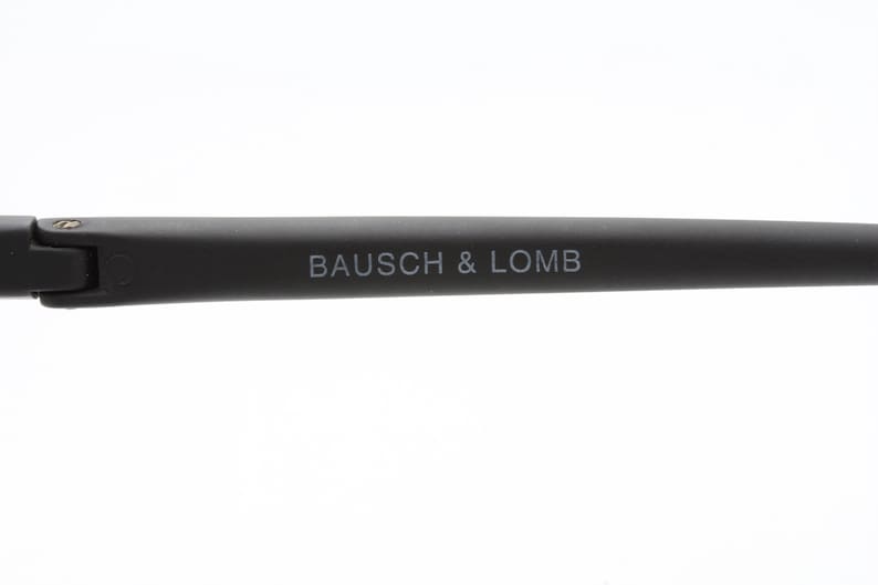 May include: Close-up of the black arm of a pair of glasses with the text "BAUSCH & LOMB" printed in white.