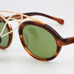 May include: Tortoise shell frame sunglasses with green lenses and a gold metal bridge. The sunglasses have a Ray-Ban logo on the side.