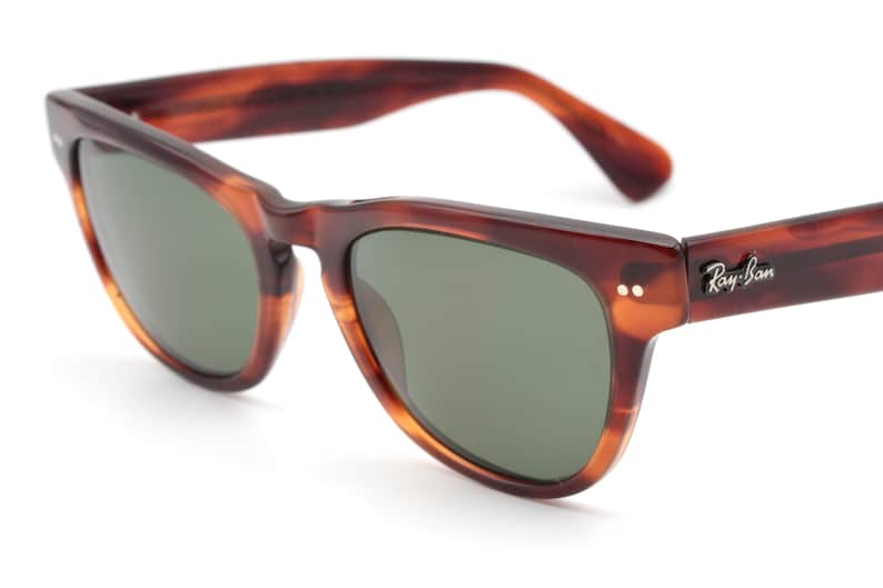 May include: Brown tortoiseshell Ray-Ban sunglasses with green lenses. The sunglasses have a classic square shape and a metal Ray-Ban logo on the right temple.