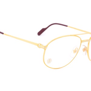 May include: Gold-tone aviator eyeglasses with clear lenses and a Cartier logo on the frame.