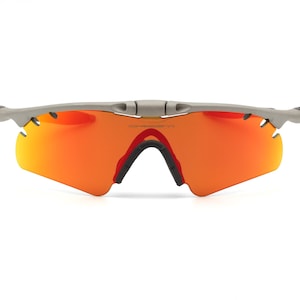 May include: Gray wraparound sunglasses with orange lenses. The sunglasses have a sporty design.