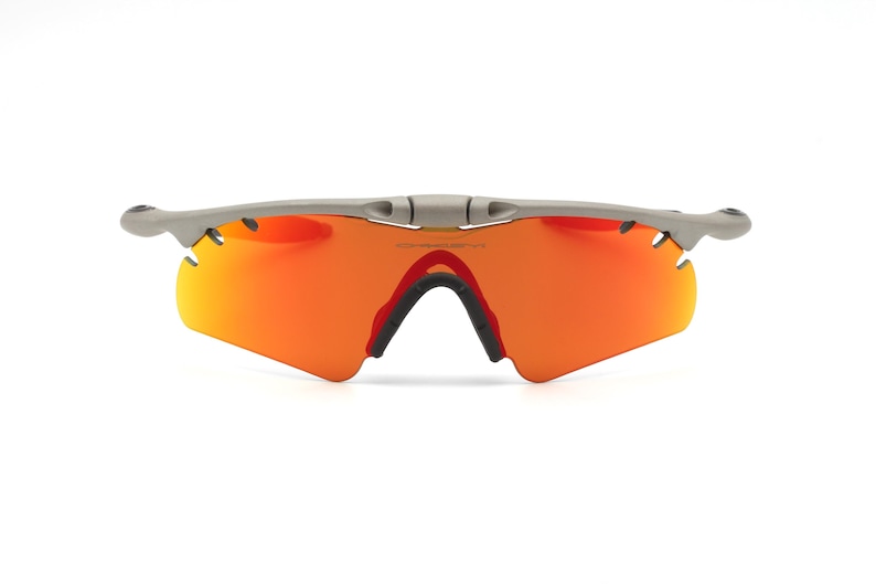 May include: Gray wraparound sunglasses with orange lenses. The sunglasses have a sporty design.
