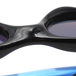 May include: Close-up of the black frame of a pair of sunglasses. The frame is curved and has a glossy finish. The lenses are dark and tinted.