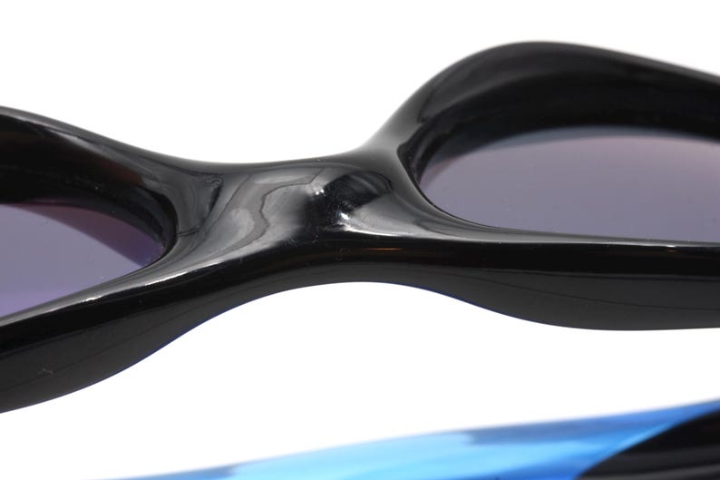 May include: Close-up of the black frame of a pair of sunglasses. The frame is curved and has a glossy finish. The lenses are dark and tinted.