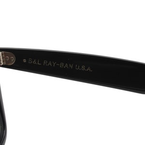 Puede incluir: Gafas de sol Ray-Ban negras con lentes verdes. Las gafas tienen una bisagra de metal y el texto "B&L RAY-BAN U.S.A." est&aacute; impreso en la patilla.