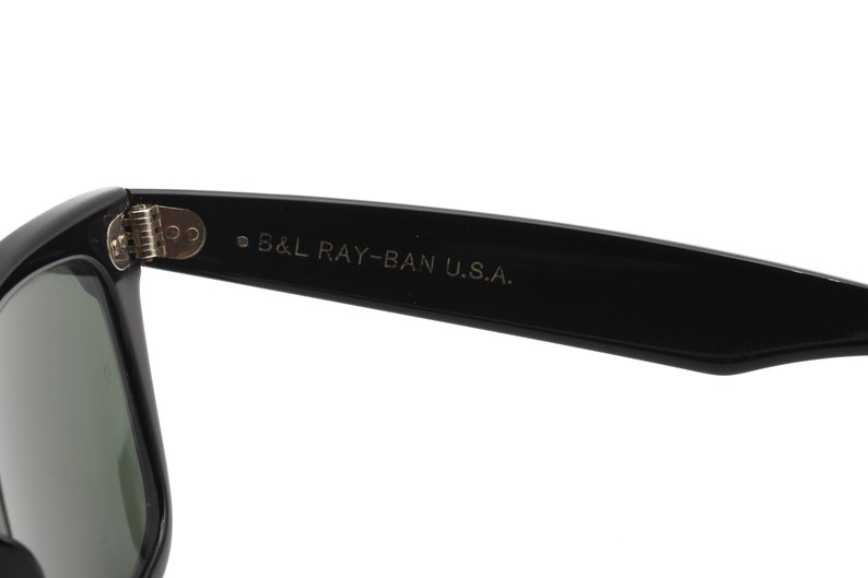Puede incluir: Gafas de sol Ray-Ban negras con lentes verdes. Las gafas tienen una bisagra de metal y el texto "B&L RAY-BAN U.S.A." est&aacute; impreso en la patilla.