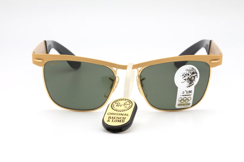 Puede incluir: Gafas de sol Ray-Ban doradas con lentes verdes y patillas negras. Las gafas tienen una etiqueta que dice "Original Bausch & Lomb" y una pegatina que dice "G-15 Lens".