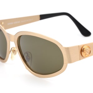 May include: Gold-toned sunglasses with a black arm and a Versace logo on the side.