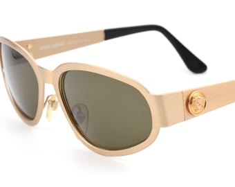 Puede incluir: Gafas de sol doradas con una patilla negra y un logotipo de Versace en el lateral.