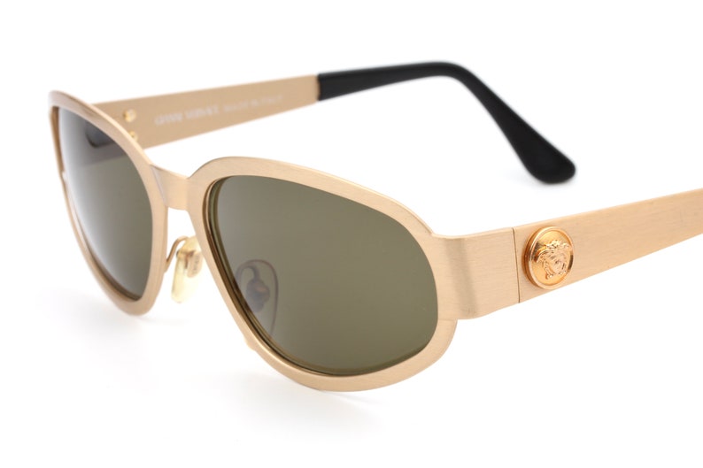 May include: Gold-toned sunglasses with a black arm and a Versace logo on the side.