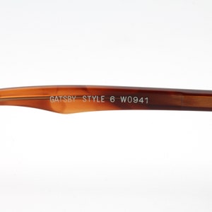 May include: Close-up of the brown tortoise shell temple arm of a pair of glasses. The arm is engraved with the text "GATSBY STYLE 6 W0941".
