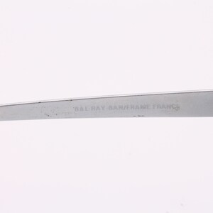 May include: Close-up of the silver metal arm of a pair of glasses with the text "BAL-RAY BAM/FRAME FRANCE" engraved on the arm.