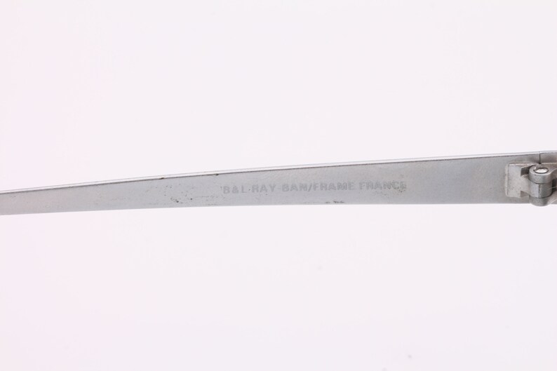 May include: Close-up of the silver metal arm of a pair of glasses with the text "BAL-RAY BAM/FRAME FRANCE" engraved on the arm.