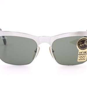 May include: Silver Ray-Ban sunglasses with green lenses and a vintage style. The sunglasses have a sticker on the right lens that says "Ray-Ban" and "G-15 Lens".