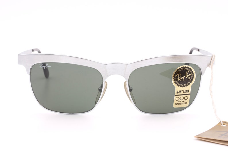 May include: Silver Ray-Ban sunglasses with green lenses and a vintage style. The sunglasses have a sticker on the right lens that says "Ray-Ban" and "G-15 Lens".