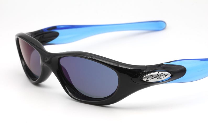 May include: Black Oakley sunglasses with blue arms and dark blue lenses. The Oakley logo is visible on the right arm.