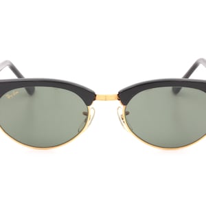 May include: Black Ray-Ban sunglasses with green lenses and gold accents. The sunglasses have a classic aviator style with a rounded shape.