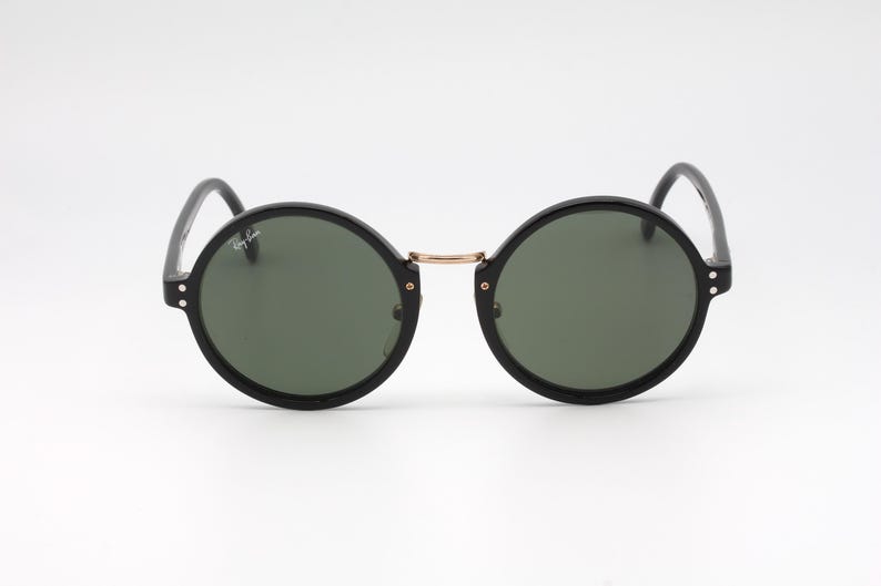 May include: Black round sunglasses with green lenses and a gold bridge.