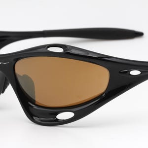 May include: Black sunglasses with brown lenses and a curved frame. The sunglasses have a small white logo on the side.
