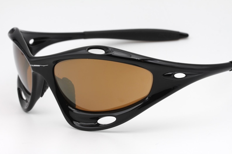 May include: Black sunglasses with brown lenses and a curved frame. The sunglasses have a small white logo on the side.