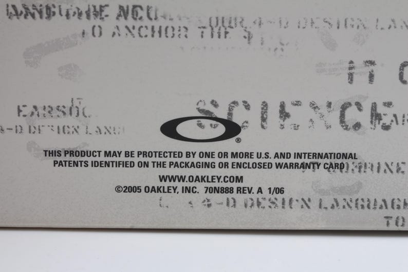 May include: A close-up of a white label with black text. The text reads "This product may be protected by one or more U.S. and international patents identified on the packaging or enclosed warranty card." The text also includes the website address "www.oakley.com" and the copyright information "&copy;2005 Oakley, Inc. 70N888 Rev. A 1/06".