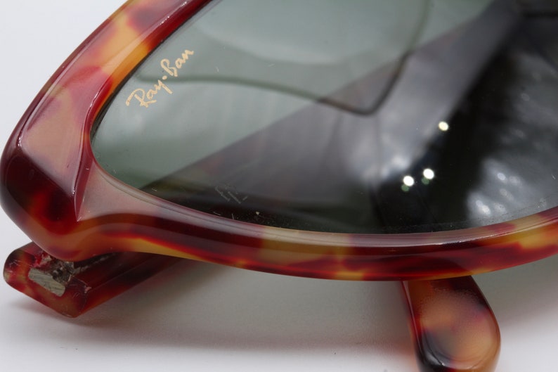 May include: Close-up of a pair of tortoiseshell Ray-Ban sunglasses. The sunglasses have a brown and gold tortoiseshell frame and green lenses. The Ray-Ban logo is visible on the right lens.
