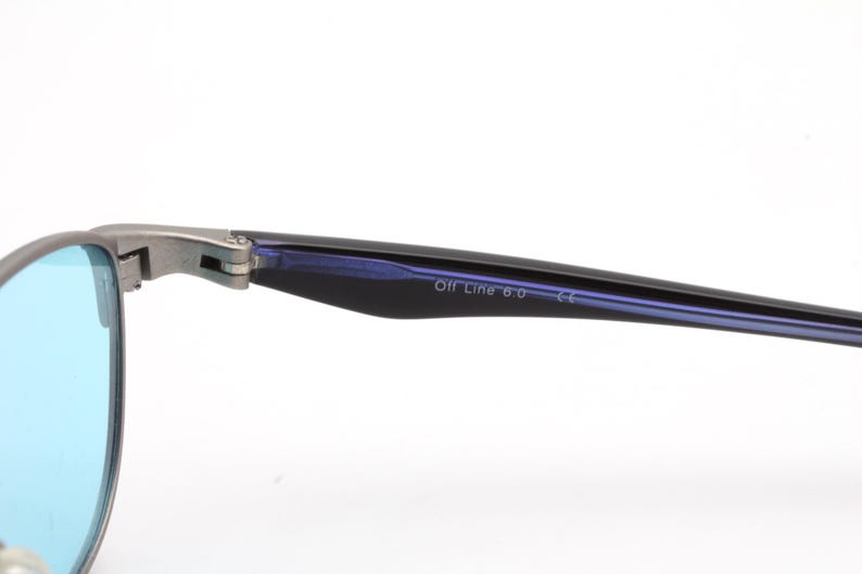 May include: Close-up of eyeglasses with blue lenses and a silver frame. The temple arm is black with the text "Off Line 6.0". The glasses are set against a white background.