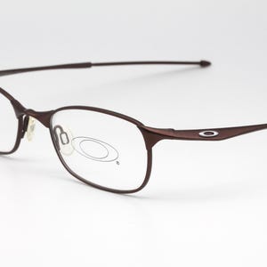 May include: Brown metal frame eyeglasses with clear lenses. The frame has a thin, wire-like design.