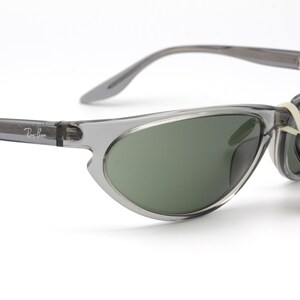 May include: Gray cat-eye sunglasses with green lenses and a Ray-Ban tag attached. The sunglasses have a clear frame.