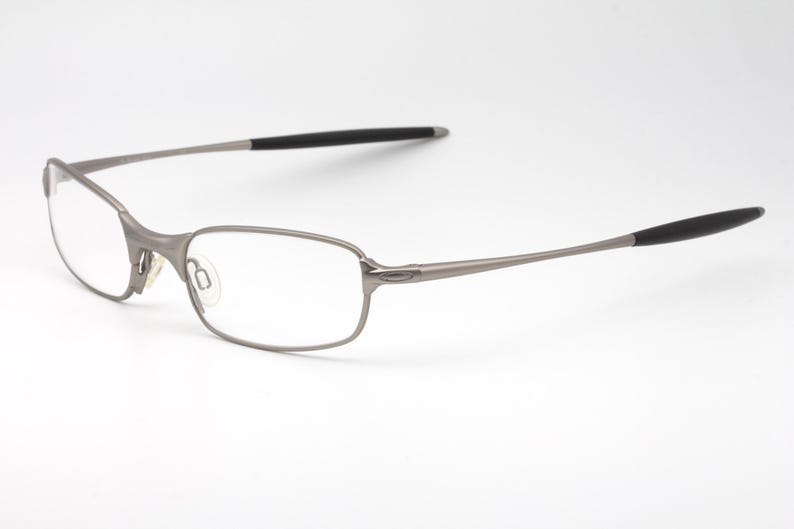 May include: A pair of eyeglasses with a silver metal frame and rectangular lenses. The temples have black rubberized tips. The glasses are set against a white background.