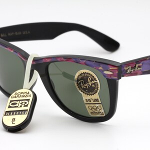 May include: Black Ray-Ban sunglasses with a floral pattern on the arms. The lenses are green and the sunglasses have a G-15 lens label. The sunglasses also have a tag that says "Doppia Garanzia" with a logo.