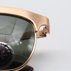 May include: Gold-tone metal frame sunglasses with green lenses. The sunglasses have a Ray-Ban logo on the left lens.