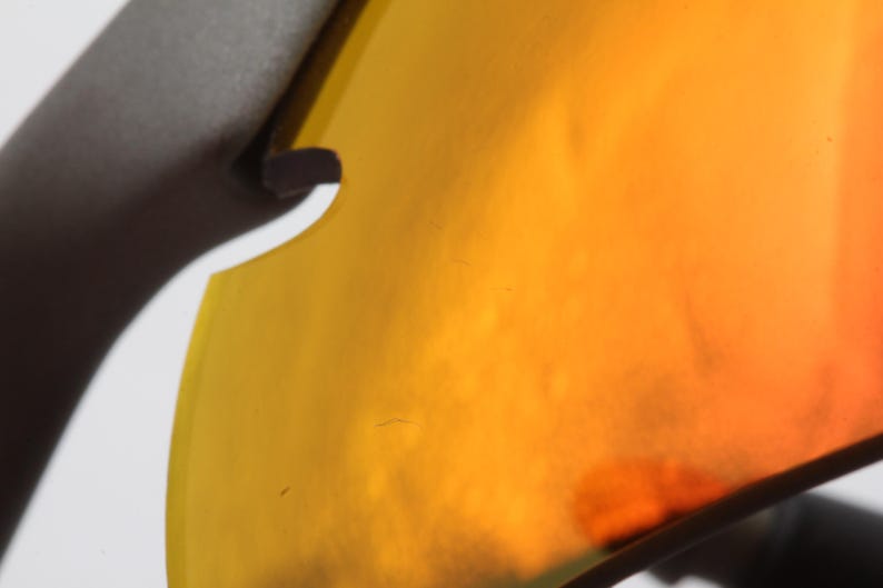 May include: Close-up of a yellow and orange tinted lens of a pair of sunglasses.