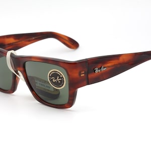 Puede incluir: Gafas de sol con estampado de carey y lentes verdes oscuras. La montura rectangular tiene patillas curvas. El logotipo de Ray-Ban est&aacute; en la patilla. Una etiqueta blanca est&aacute; adherida a la montura.
