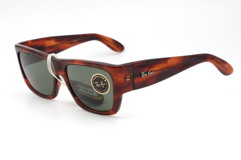 Puede incluir: Gafas de sol con estampado de carey y lentes verdes oscuras. La montura rectangular tiene patillas curvas. El logotipo de Ray-Ban est&aacute; en la patilla. Una etiqueta blanca est&aacute; adherida a la montura.