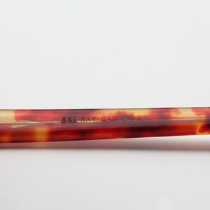 May include: Close-up of the brown tortoiseshell arm of a pair of glasses with the text "B&L Ray-Ban USA" printed on the arm.