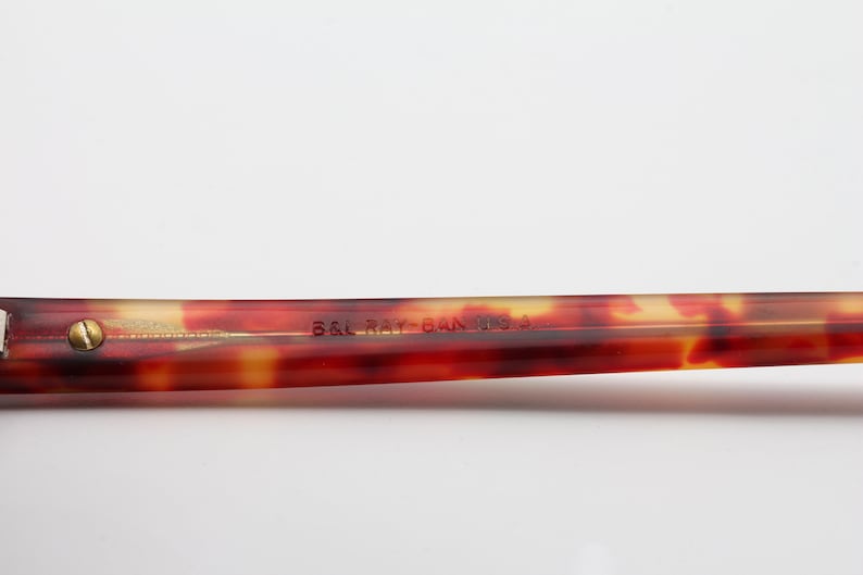 May include: Close-up of the brown tortoiseshell arm of a pair of glasses with the text "B&L Ray-Ban USA" printed on the arm.