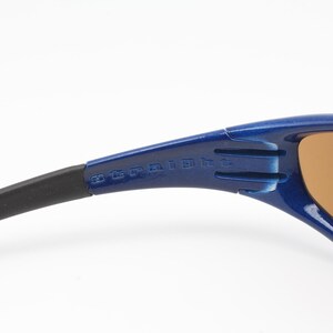 May include: Blue and black wraparound sunglasses with brown lenses. The sunglasses have the text "20 CE UV 400" printed on the side.