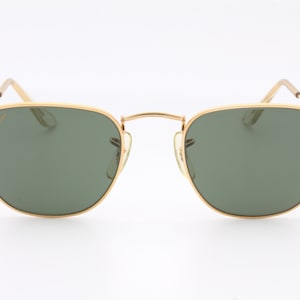 May include: Gold-framed sunglasses with green lenses. The sunglasses have a classic, rectangular shape.