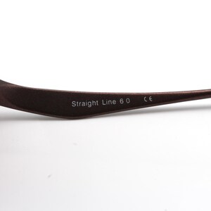 May include: Close-up of the brown metal arm of a pair of glasses with the text "Straight Line 6.0 CE" printed on it.