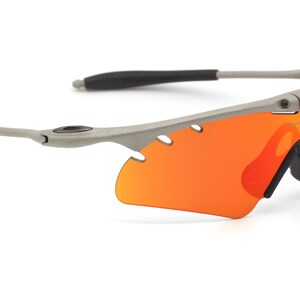 May include: Gray wraparound sunglasses with orange lenses. The sunglasses have a sporty design and are made of durable materials.