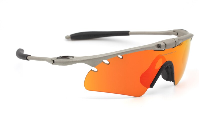 May include: Gray wraparound sunglasses with orange lenses. The sunglasses have a sporty design and are made of durable materials.