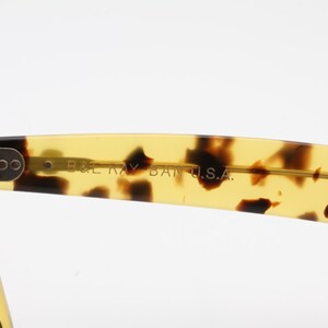 Puede incluir: Primer plano de gafas de sol con montura de carey. El texto "B&L RAY BAN U.S.A." es visible en la patilla. Las lentes son de color gris oscuro. Dise&ntilde;o cl&aacute;sico.