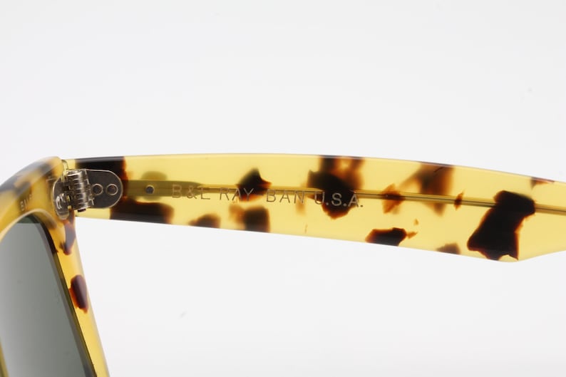 Puede incluir: Primer plano de gafas de sol con montura de carey. El texto "B&L RAY BAN U.S.A." es visible en la patilla. Las lentes son de color gris oscuro. Dise&ntilde;o cl&aacute;sico.