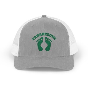 May include: A grey trucker cap with a white mesh back. The front displays the word "PARARESCUE" in green above two green footprints.