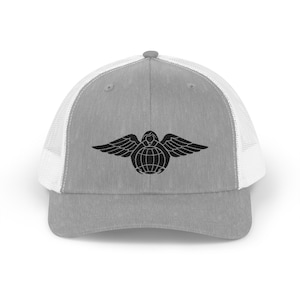 May include: Gray trucker hat with a white mesh back and a black emblem featuring a winged figure over a globe. The hat has a curved brim and a snap closure for adjustable sizing.