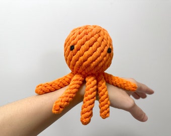 May include: Orange rope octopus toy with black eyes. The toy is made of tightly woven rope and has eight tentacles.