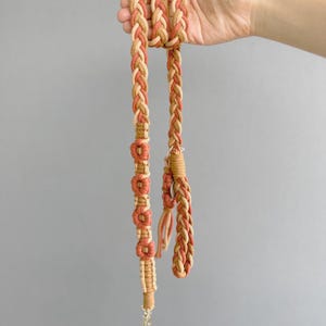 May include: A braided dog leash with a brown and orange color scheme. The leash has a flower pattern on one side and a simple braid on the other.